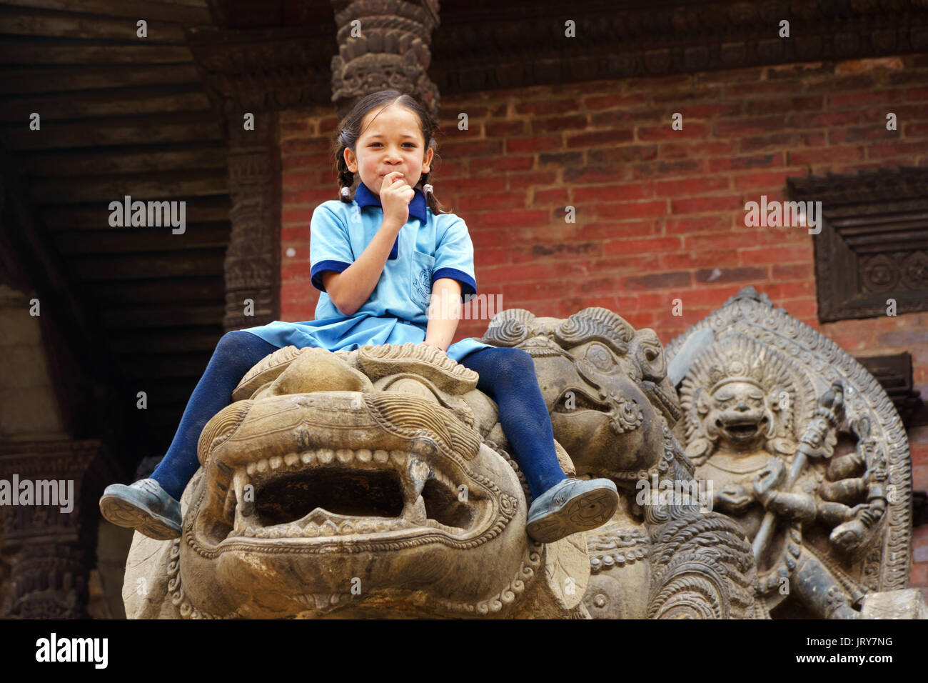 Young Nepalese girl sitting on the statue of a lion in Bhaktapur. Stock Photo