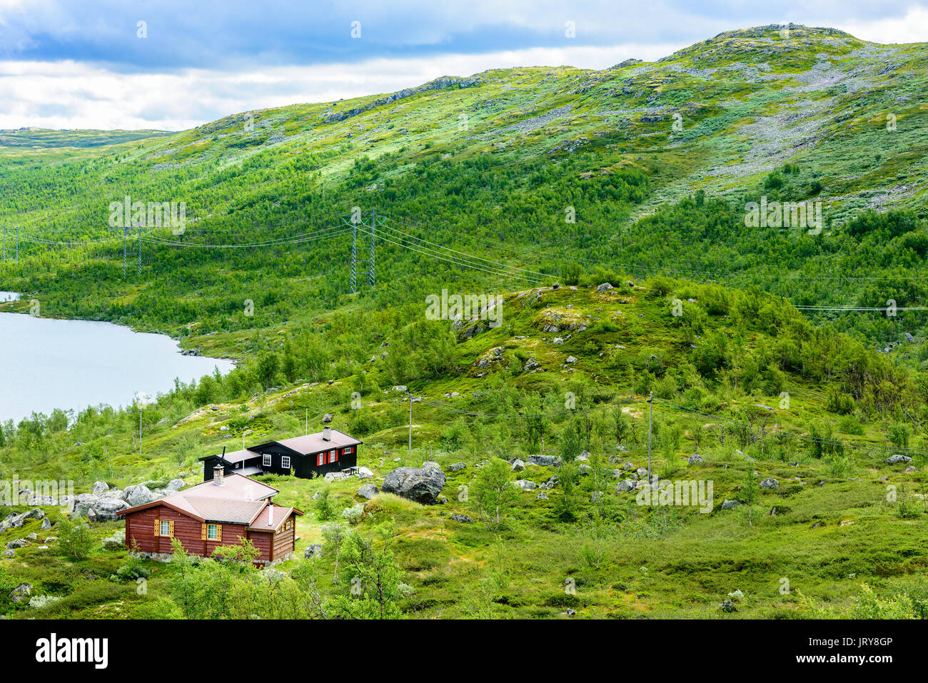 Group of small lakeside cabins in mountainous landscape powerlines on the mountainside mountain peak in background location hardangervidda in norwa