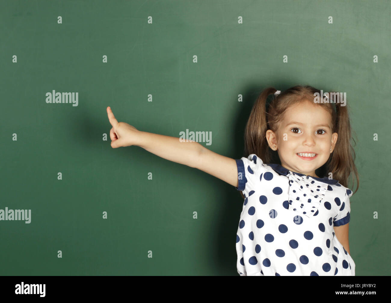 Smiling child girl show with a finger blank school blackboard Stock Photo