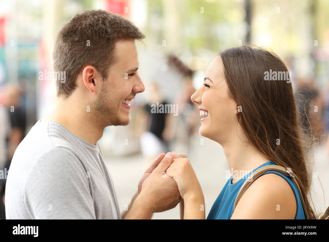 Happy couple in love looking each other laughing and holding hands on the street Stock Photo