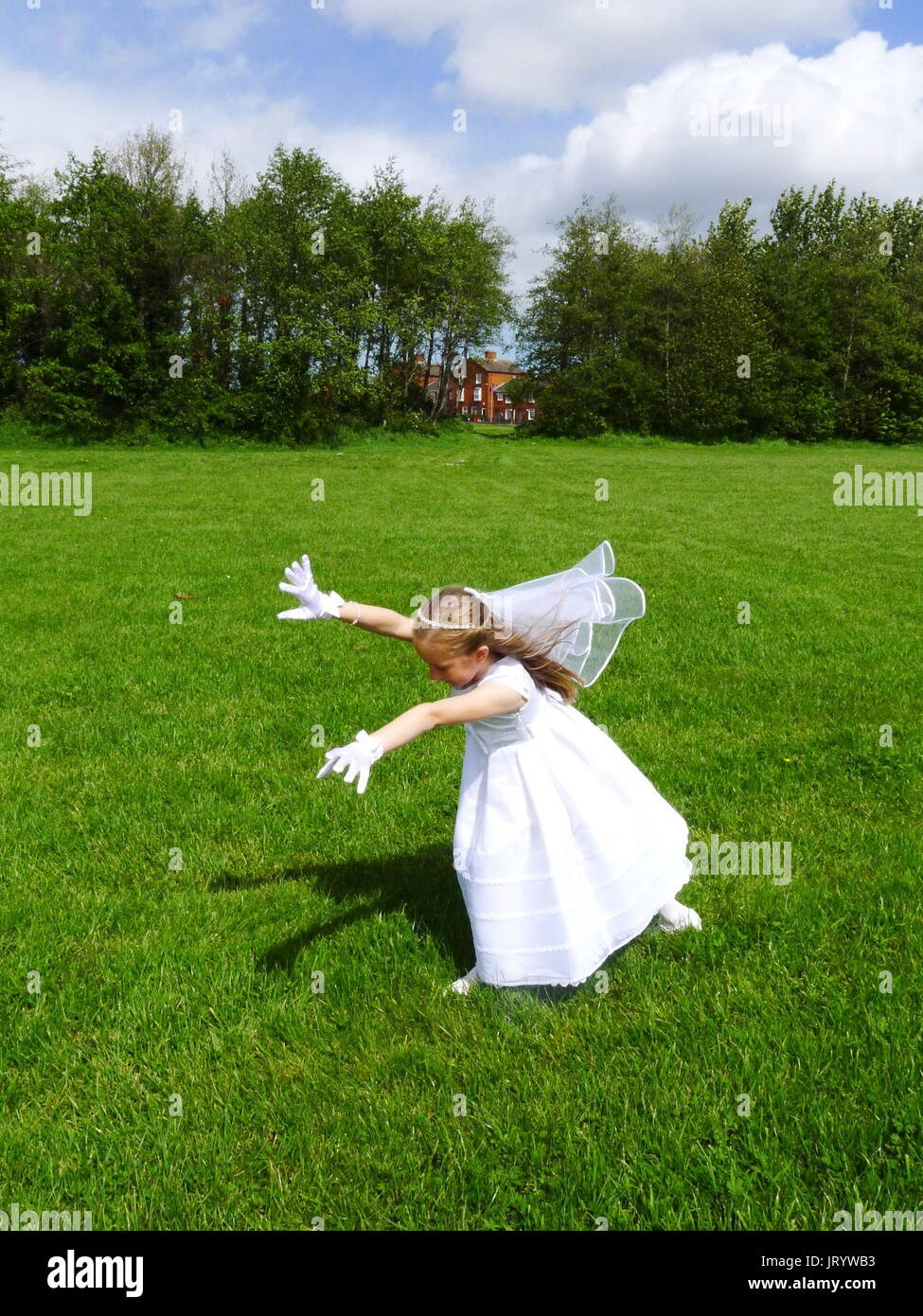 First Holy Communion Girl in her white dress and veil doing a cartwheel kids park, joyful, joy concept, happiness, carefree, freedom, day Stock Photo