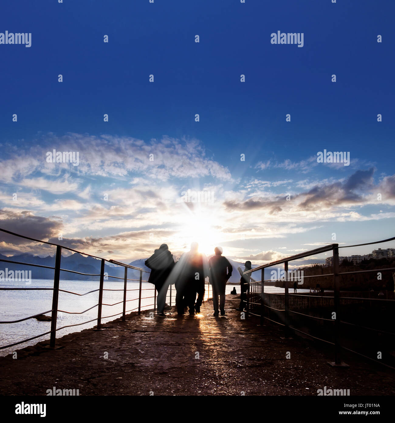 silhouetted people walking on street over sunset sky with sunbeam Stock ...