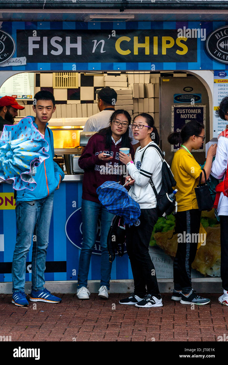 Young Tourists Shelter From The Rain Outside A Fish and Chip Shop On Brighton Seafront, Brighton, Sussex, UK Stock Photo