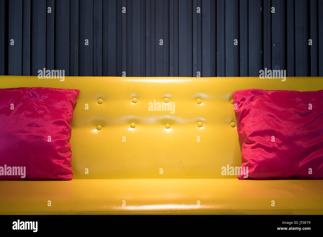 yellow leather sofa with pink fabric pillow beside black wall Stock Photo