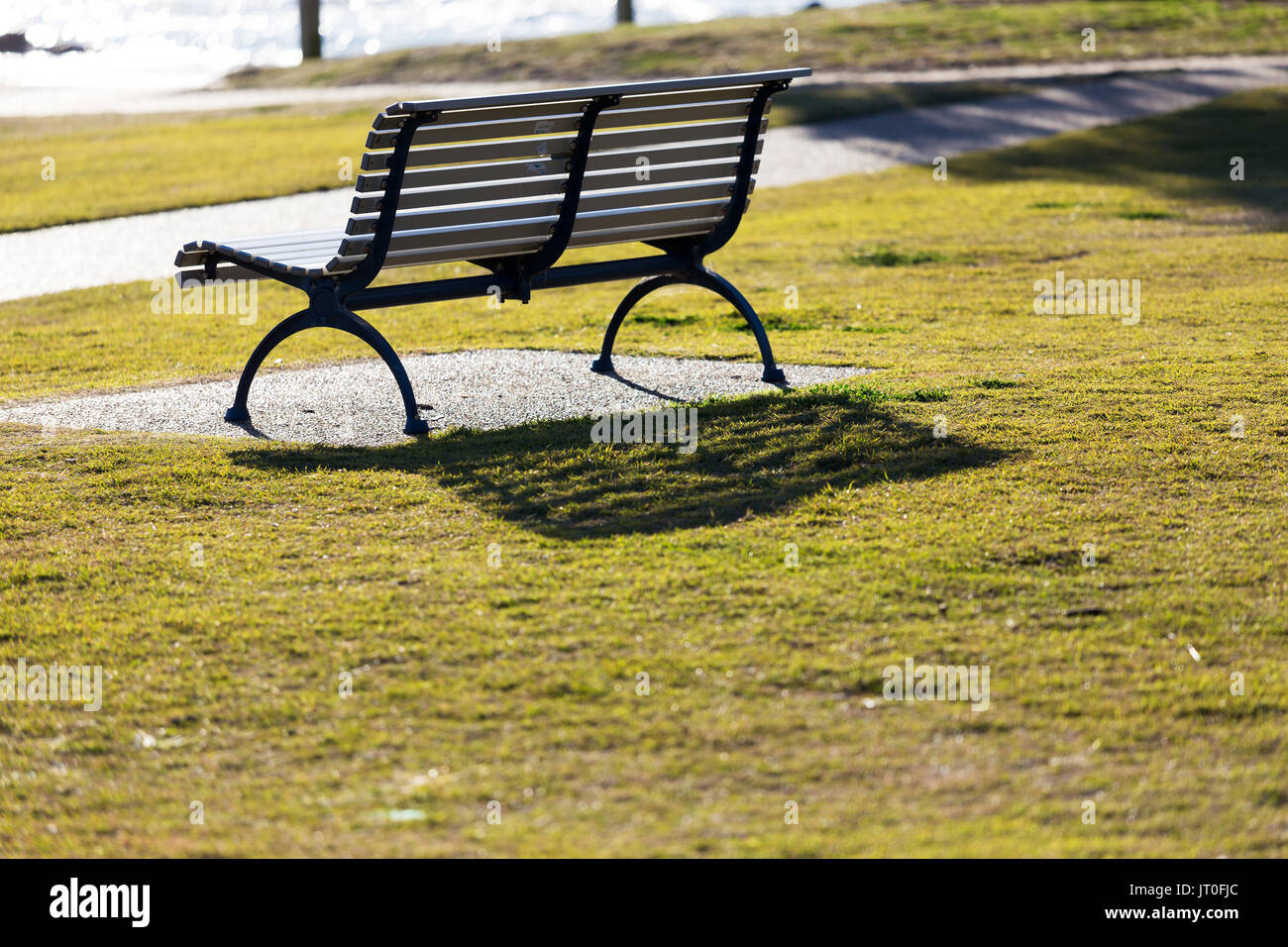 An empty park seat by the sea and beach, backlit by vibrant, bright morning sun light with no people in sight. Stock Photo