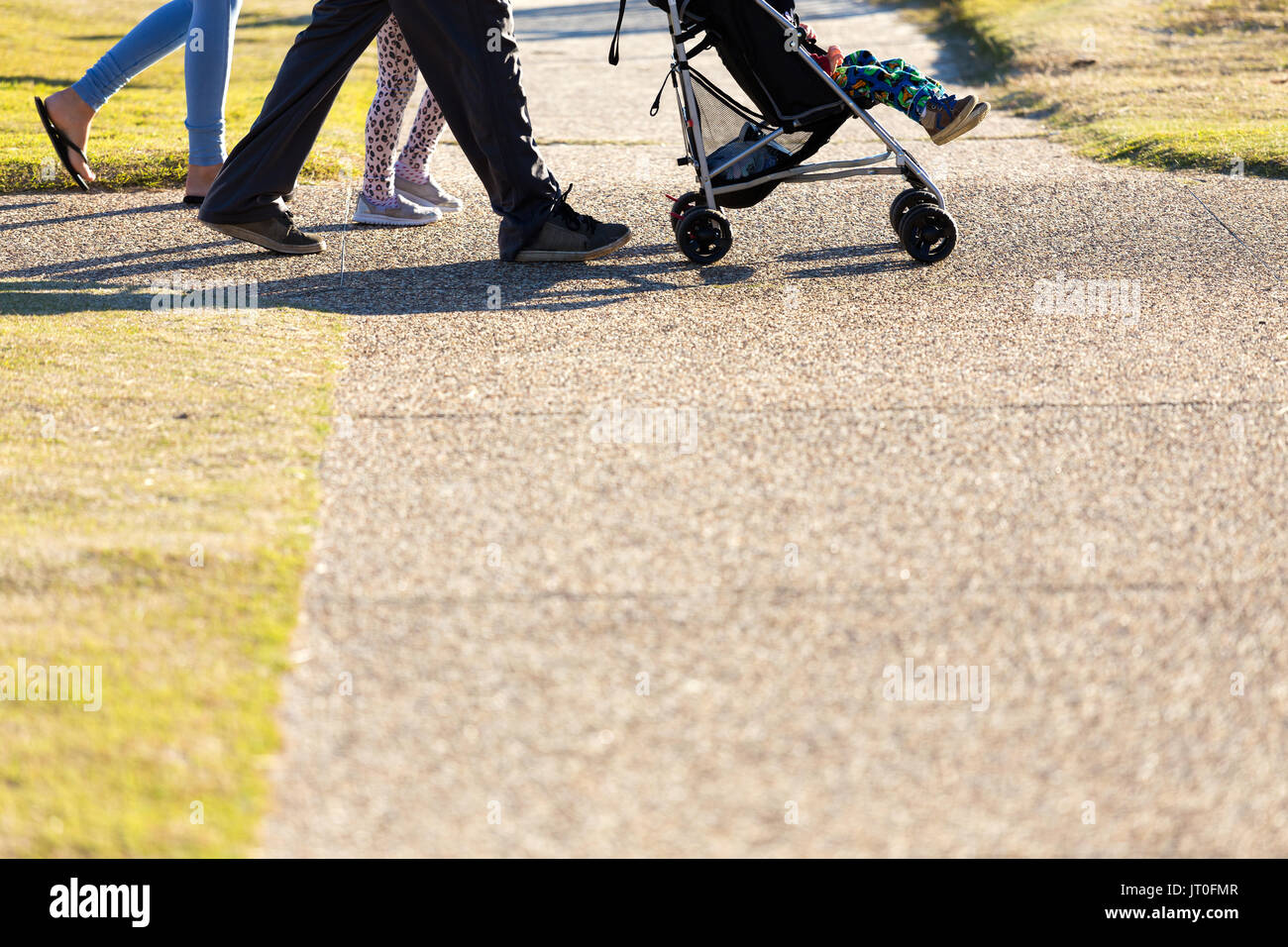 A below waist shot of a family of four, including a baby in a pram, walking and exercising on a city park footpath. Stock Photo