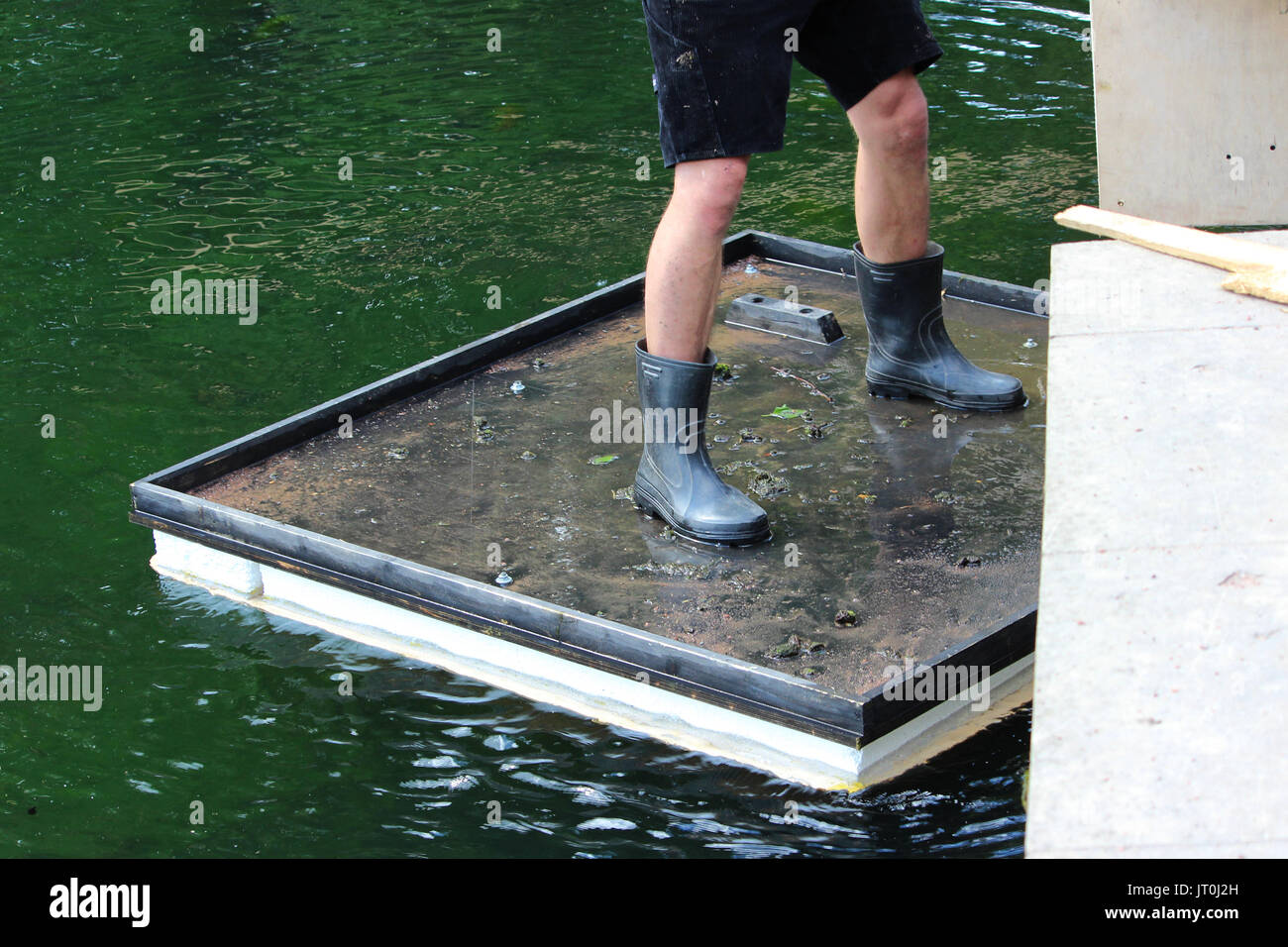 Square raft for bridge repair works floats on the water. The worker is