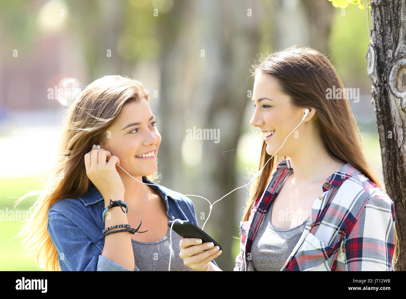 Two happy friends sharing on line music with ear buds outdoors in a park Stock Photo