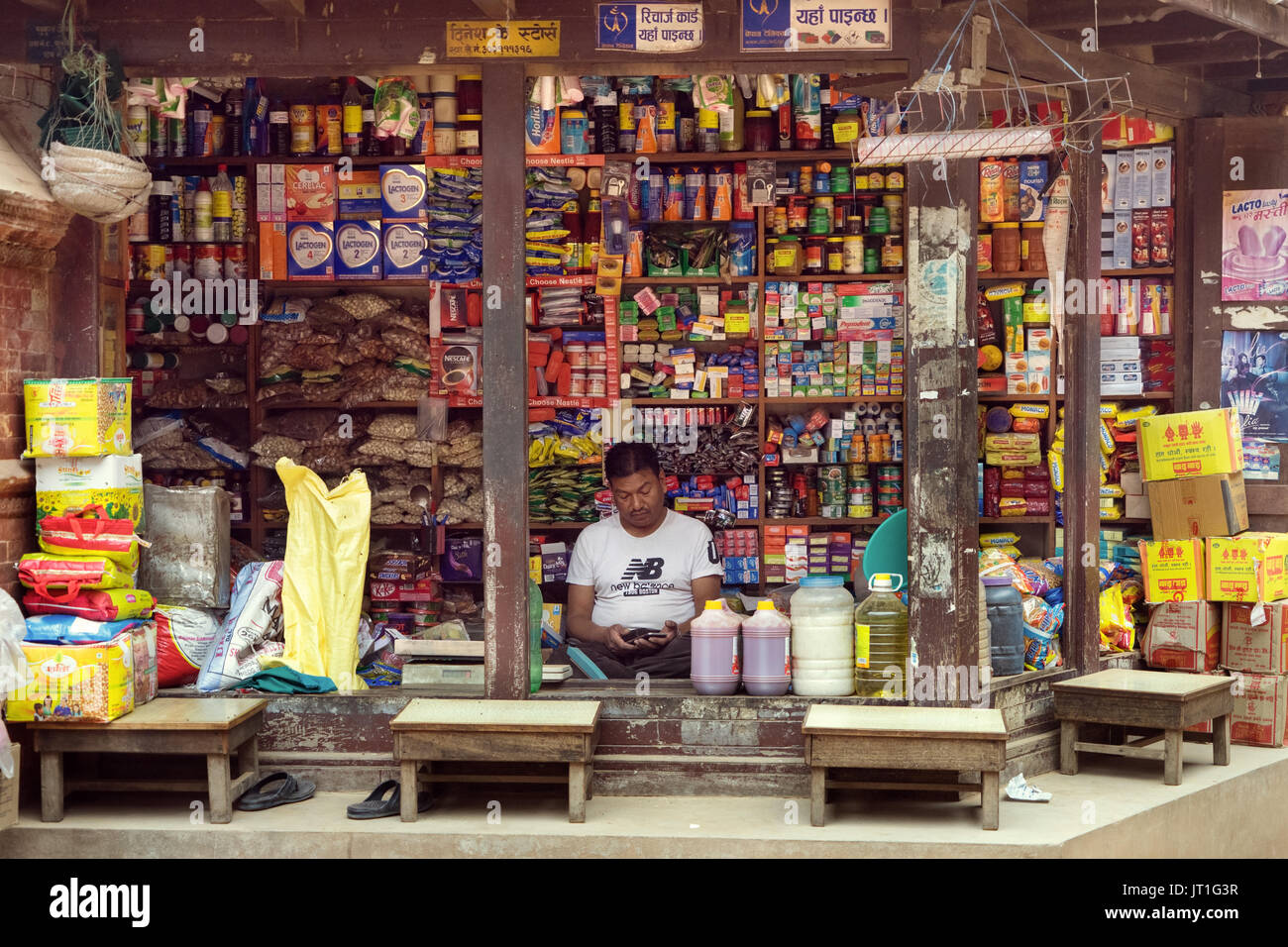 Grocery store vendor looking at his mobile phone. Bhaktapur, Nepal