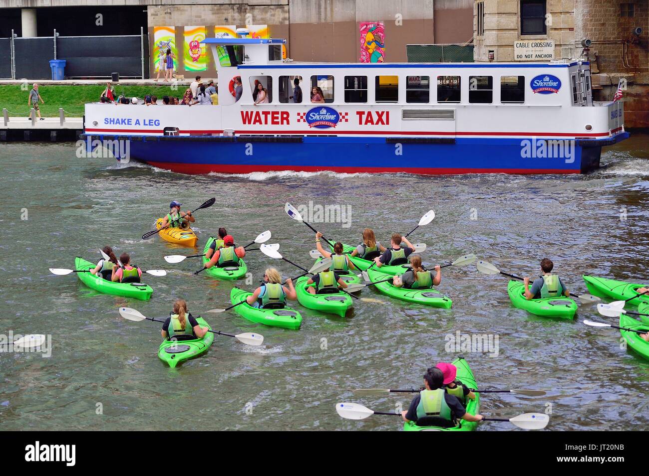 Chicago, Illinois, USA. As a water taxi passes, a group of kayakes paddle across the Chicago River. Stock Photo