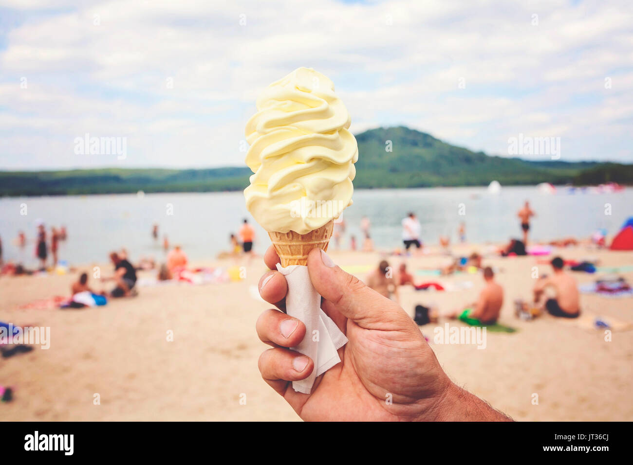 Male hand holding Vanilla Ice Cream in hot weather by the lake beach