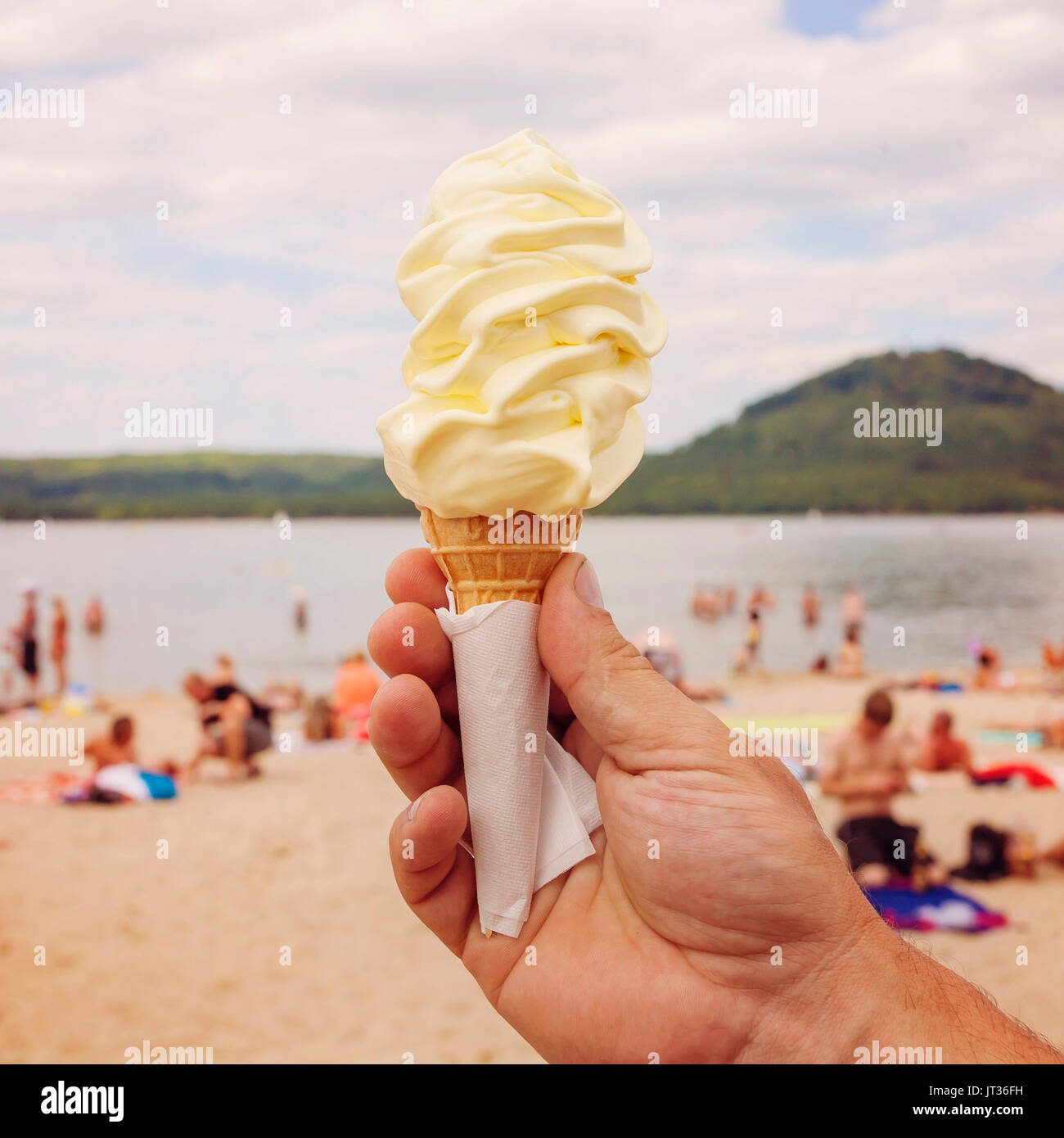 Male hand holding Vanilla Ice Cream in hot weather by the lake beach