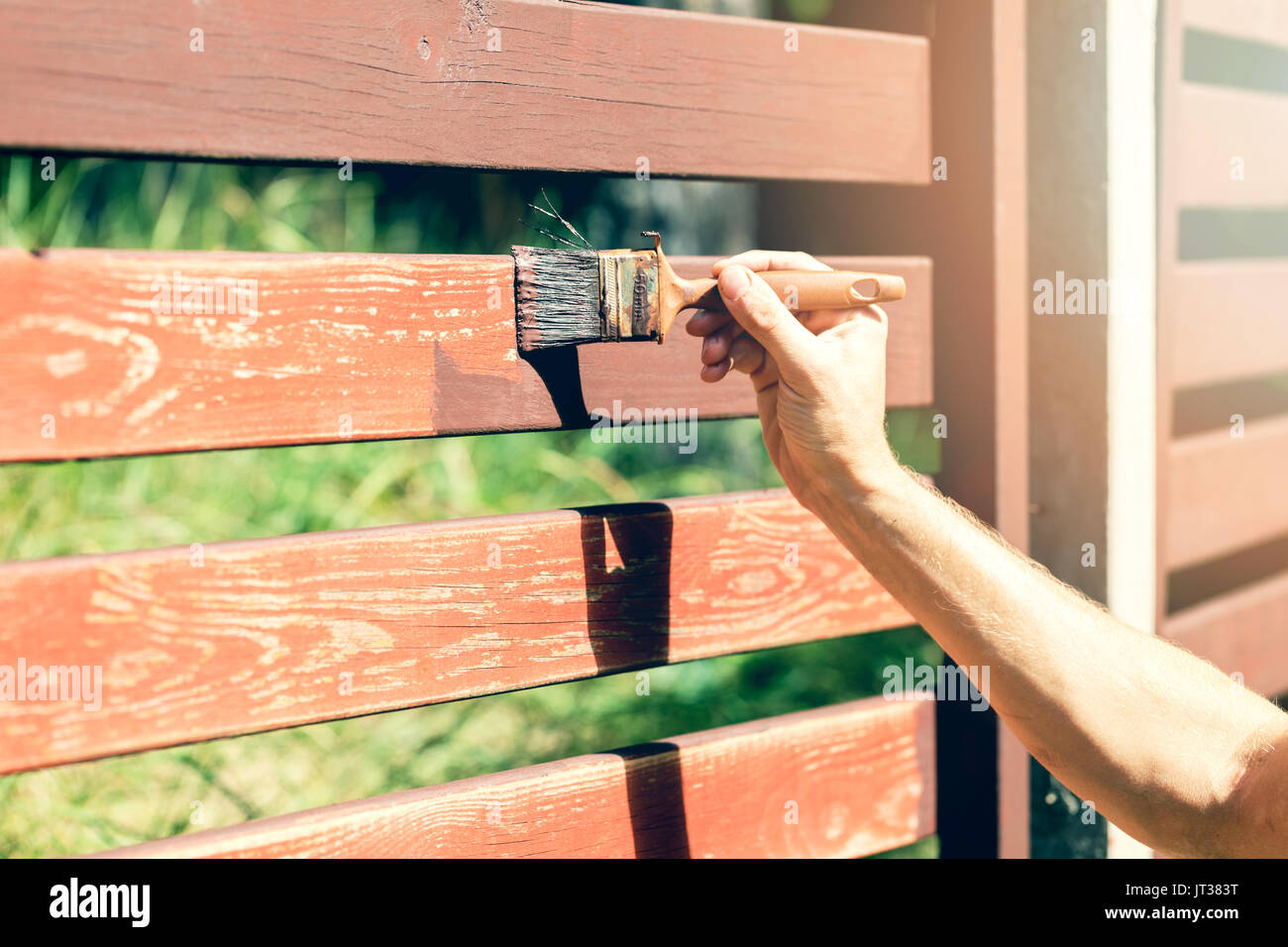 hand with paintbrush painting wooden fence with brown paint Stock Photo