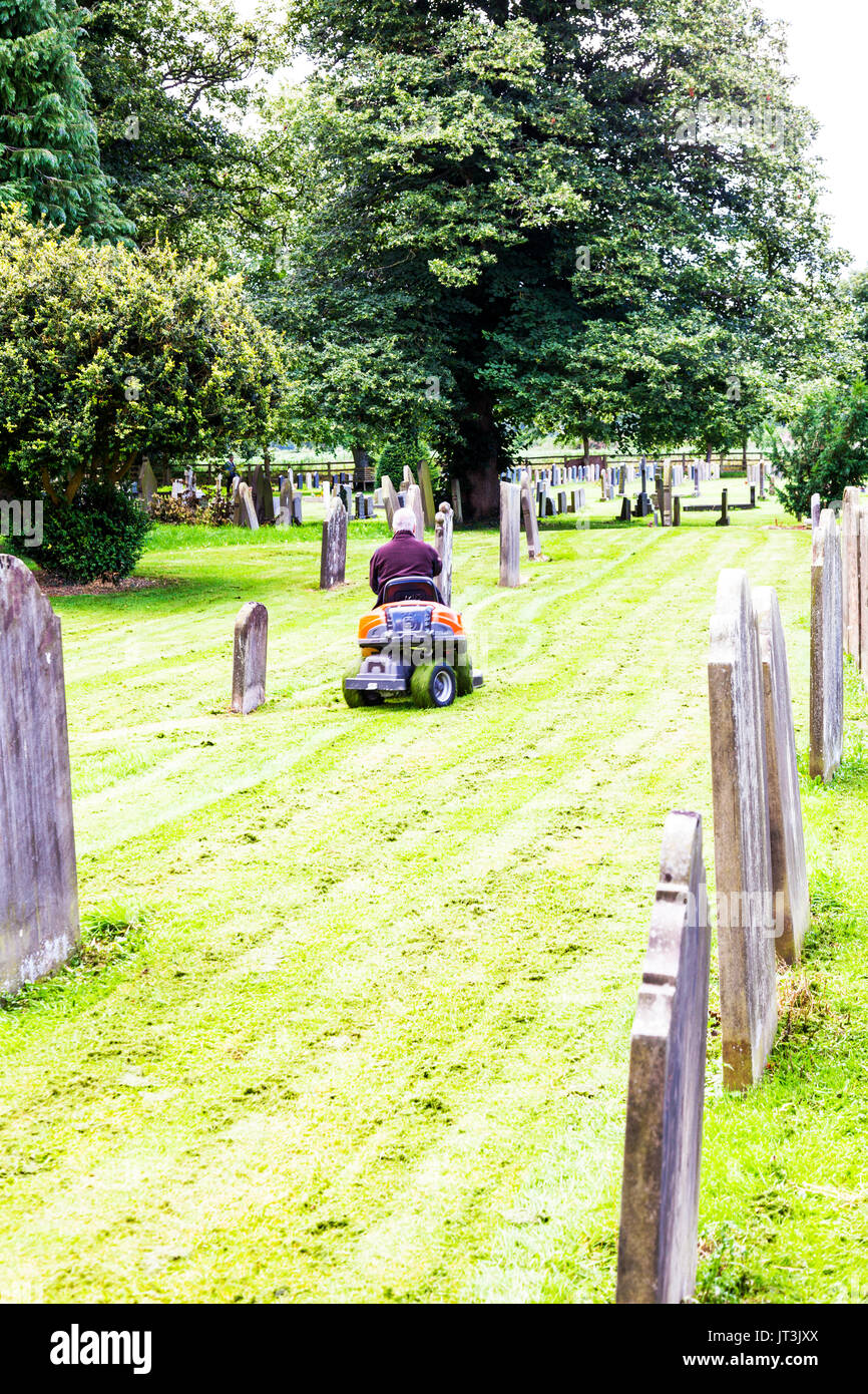 Cutting grass at graveyard, graveyard grass cutting, ride on lawnmower, using ride on lawnmower, mowing grass at graveyard, graveyards mowing, UK Stock Photo
