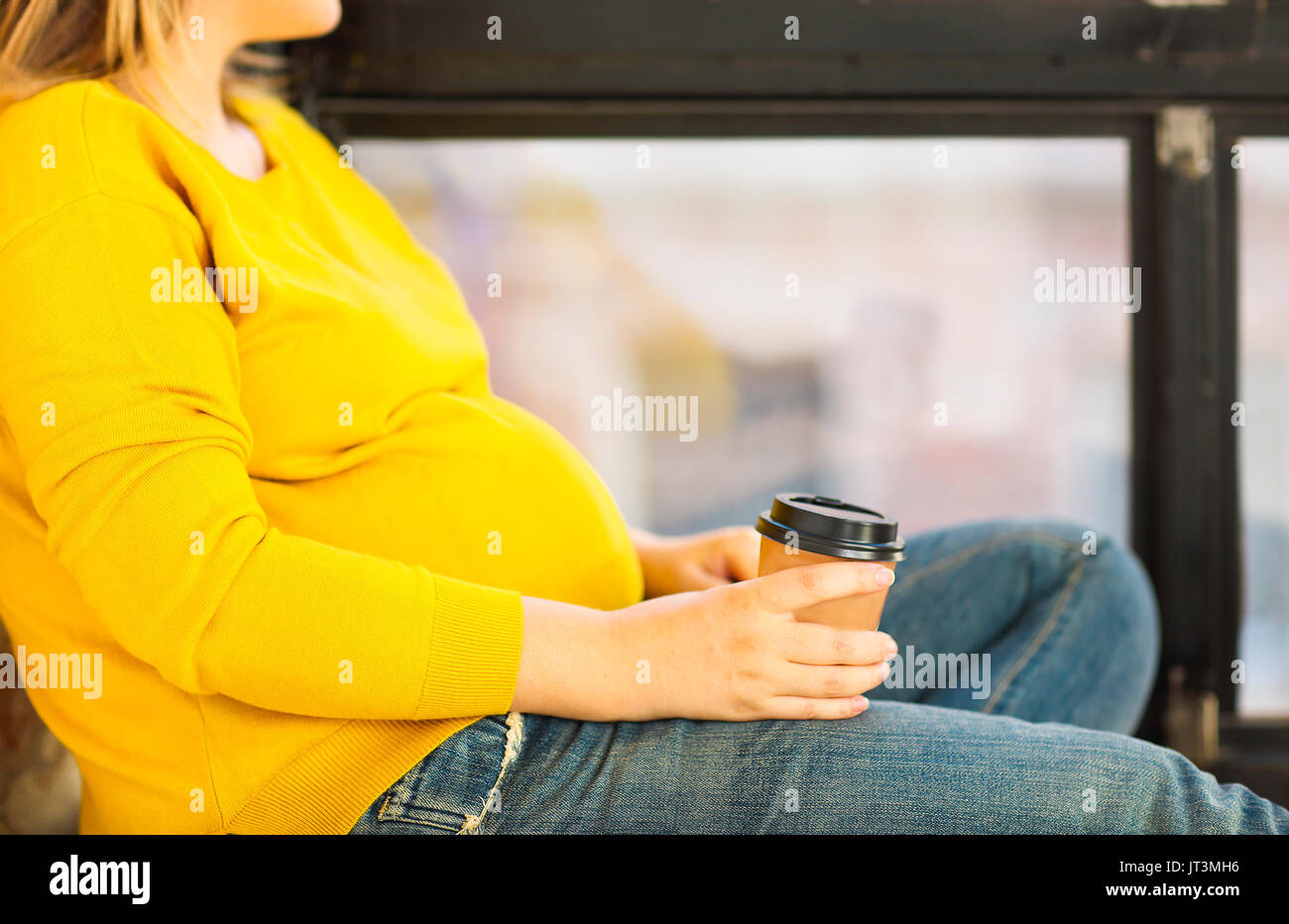 Young pregnant woman sitting near window with cup of coffee Stock Photo ...
