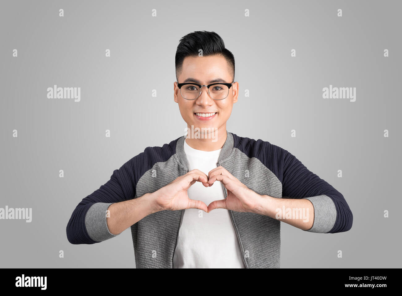 Closeup portrait handsome smiling young business man makes the heart using fingers, hands, isolated grey wall background. Positive human emotions, fac Stock Photo