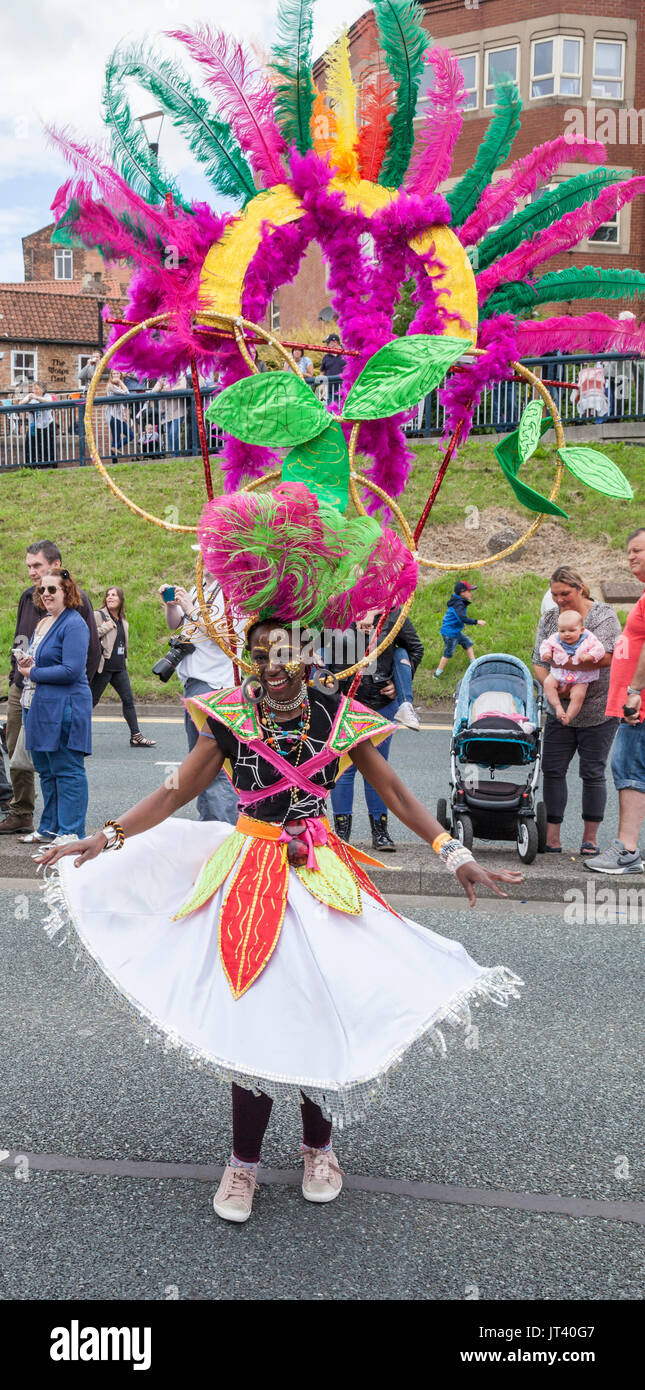 A young black woman in colourful head dress dances along the road at the Stockton International Riverside Festival Parade Stock Photo