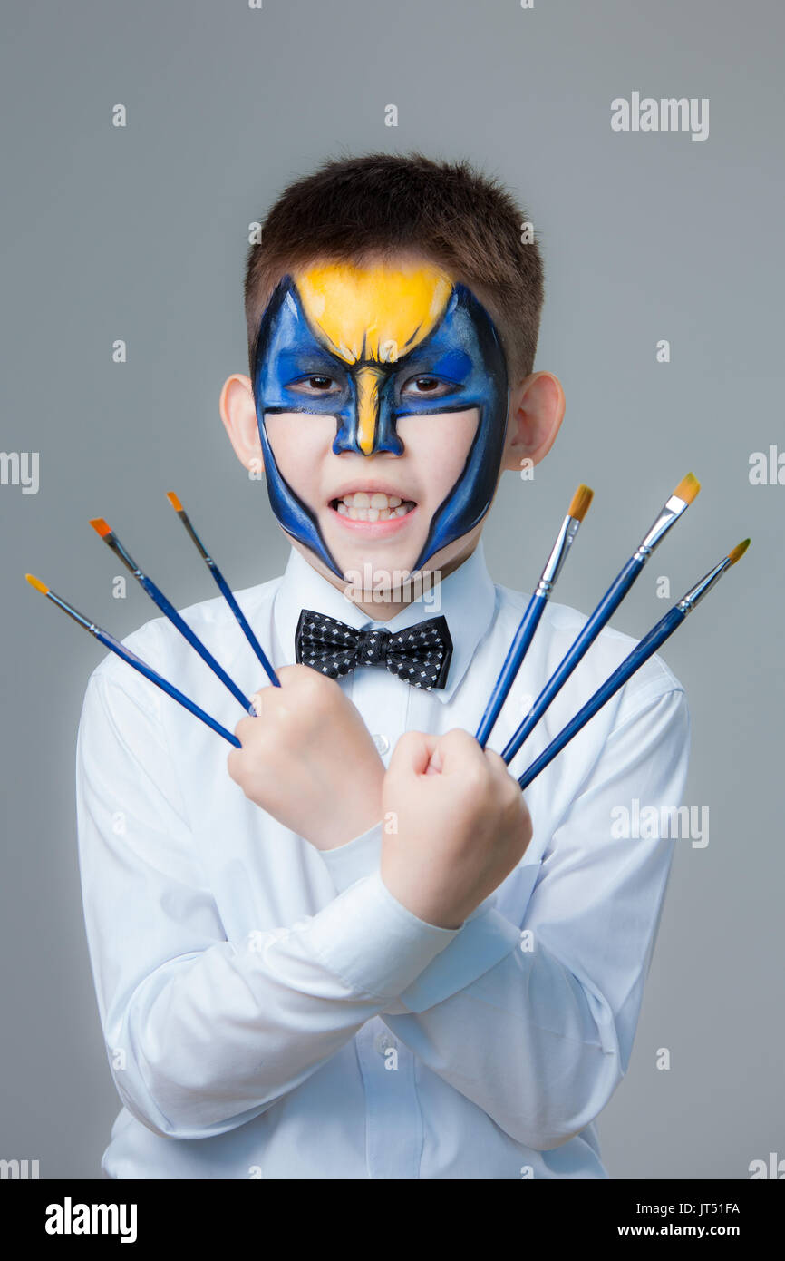 Little boy with paintings on his face Wolverine with brushes in hands Stock Photo