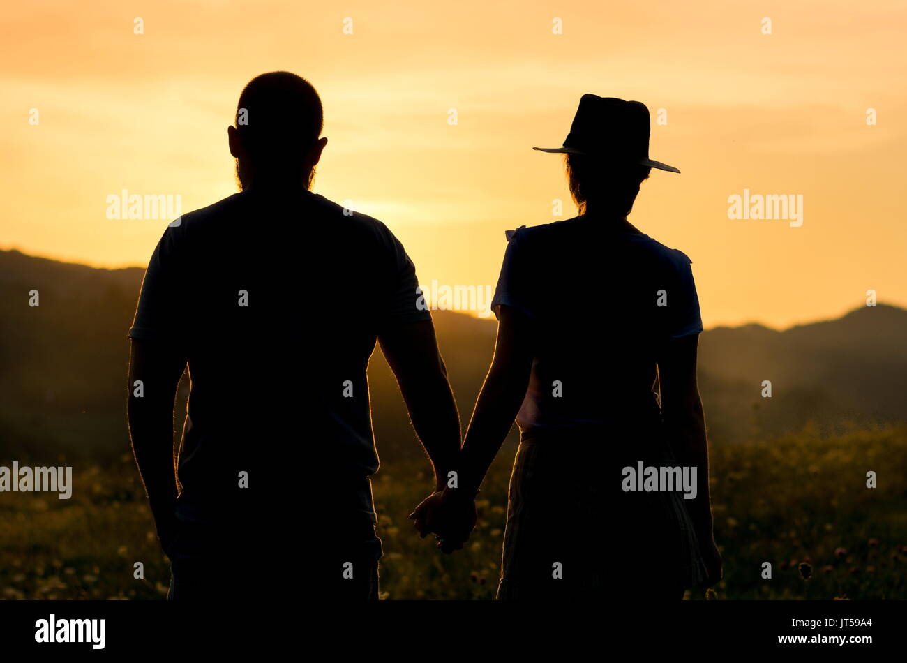 Couple holding hands and watching the sunset, romantic silhouette Stock Photo