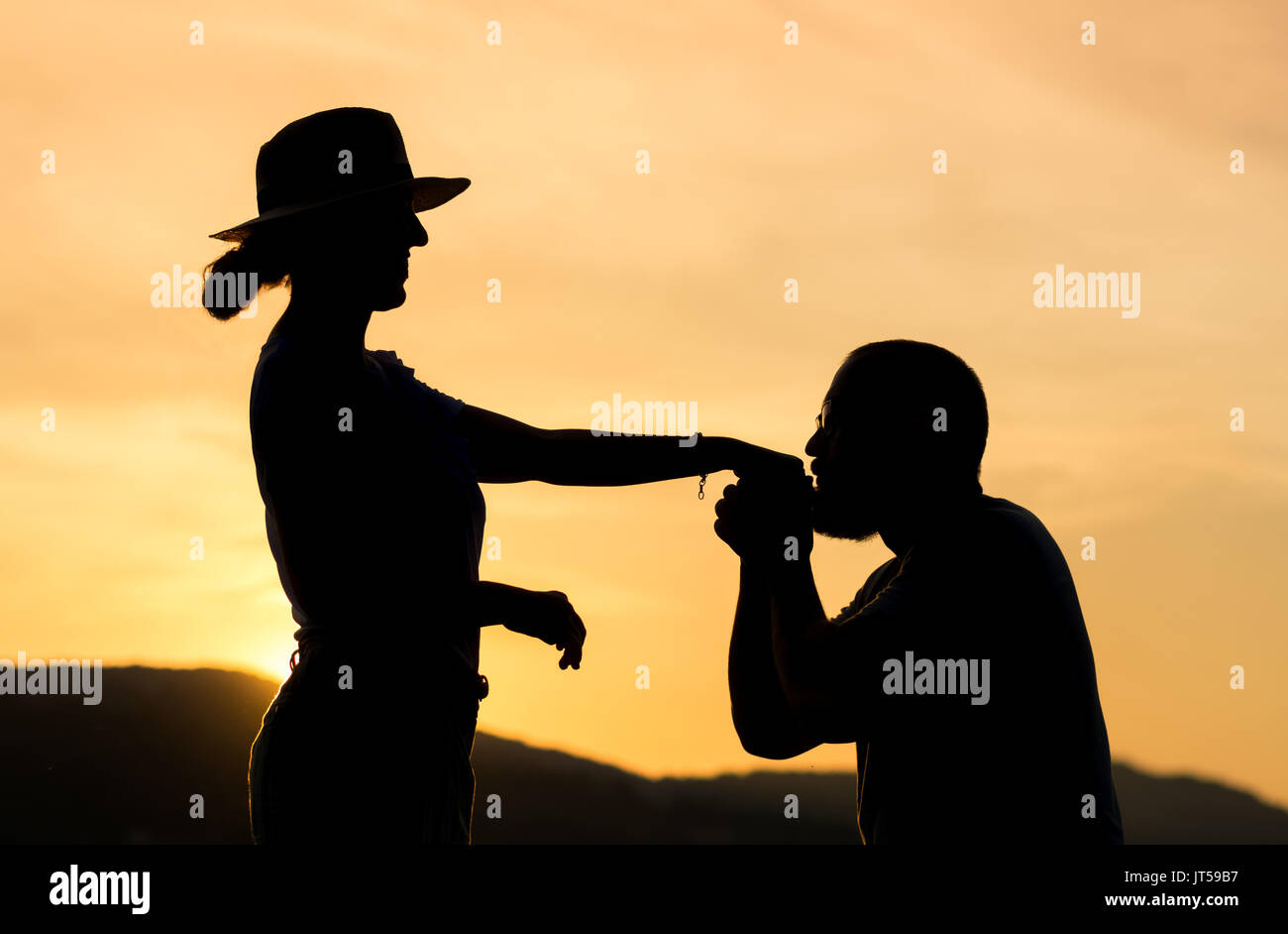 Silhouette of a gentleman kissing hand of his date at sunset Stock Photo