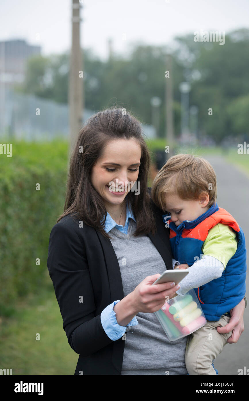 Working Mother holding baby and using mobile phone in street. Stock Photo
