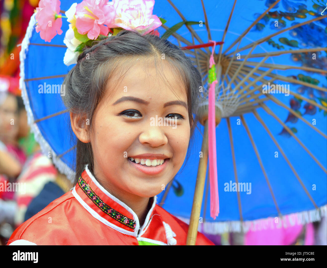 Pretty Thai Chinese girl in traditional dress with blue parasol smiles for the camera. Stock Photo