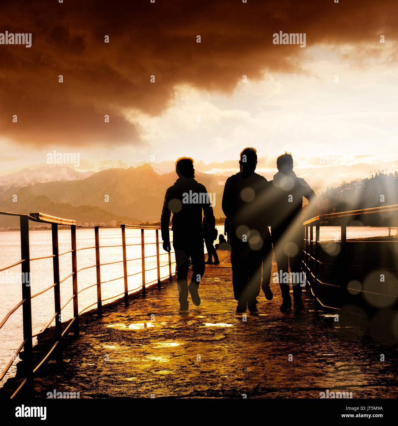 silhouetted people walking on street over sunset sky with sunbeam Stock ...