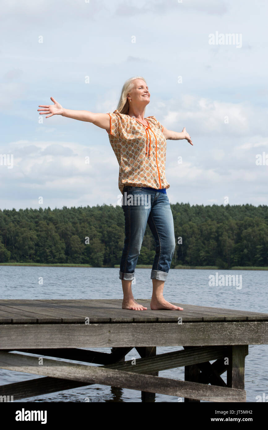 Woman standing on a landing stage and spreading her arms Stock Photo