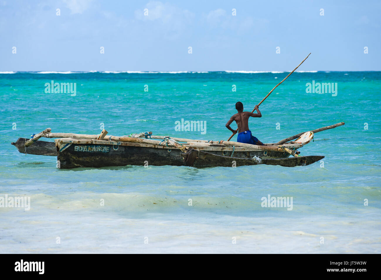 Fisherman in traditional dhow fishing boat taking it out to sea with wooden pole, Diani, Kenya Stock Photo