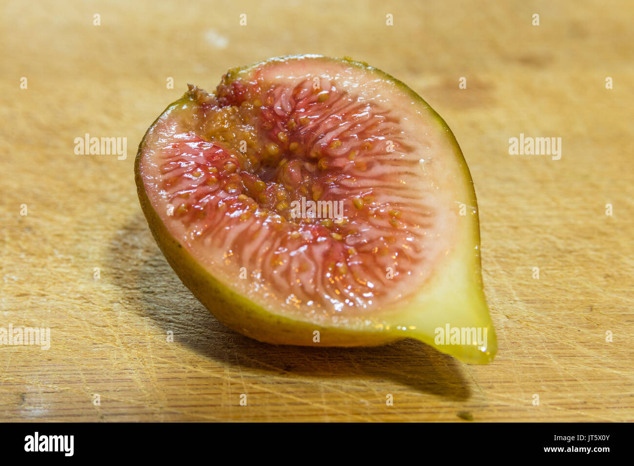 Horizontal photo of a close up on a half of a cut fig on a wooden ...