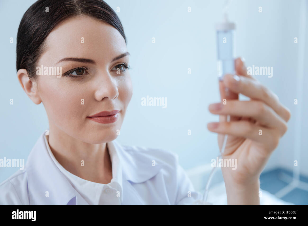 Pleasant professional nurse looking at the IV drip bottle Stock Photo