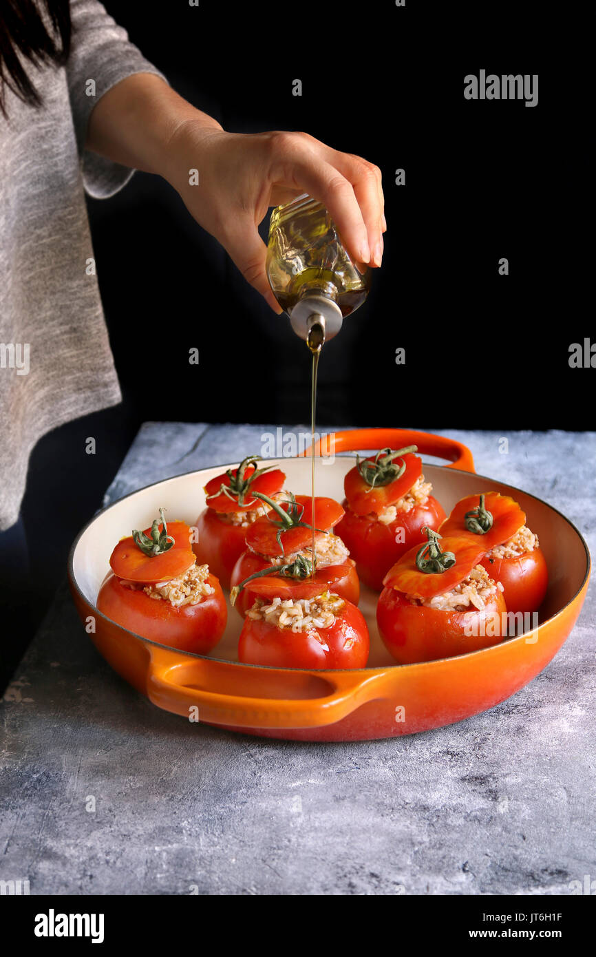 Female hand pouring olive oil over stuffed tomatoes with ground beef
