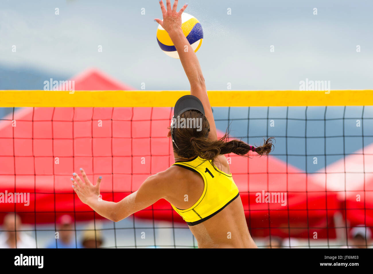 Volleyball player is a female beach volleyball player jumping at the net to spike the ball down. Stock Photo