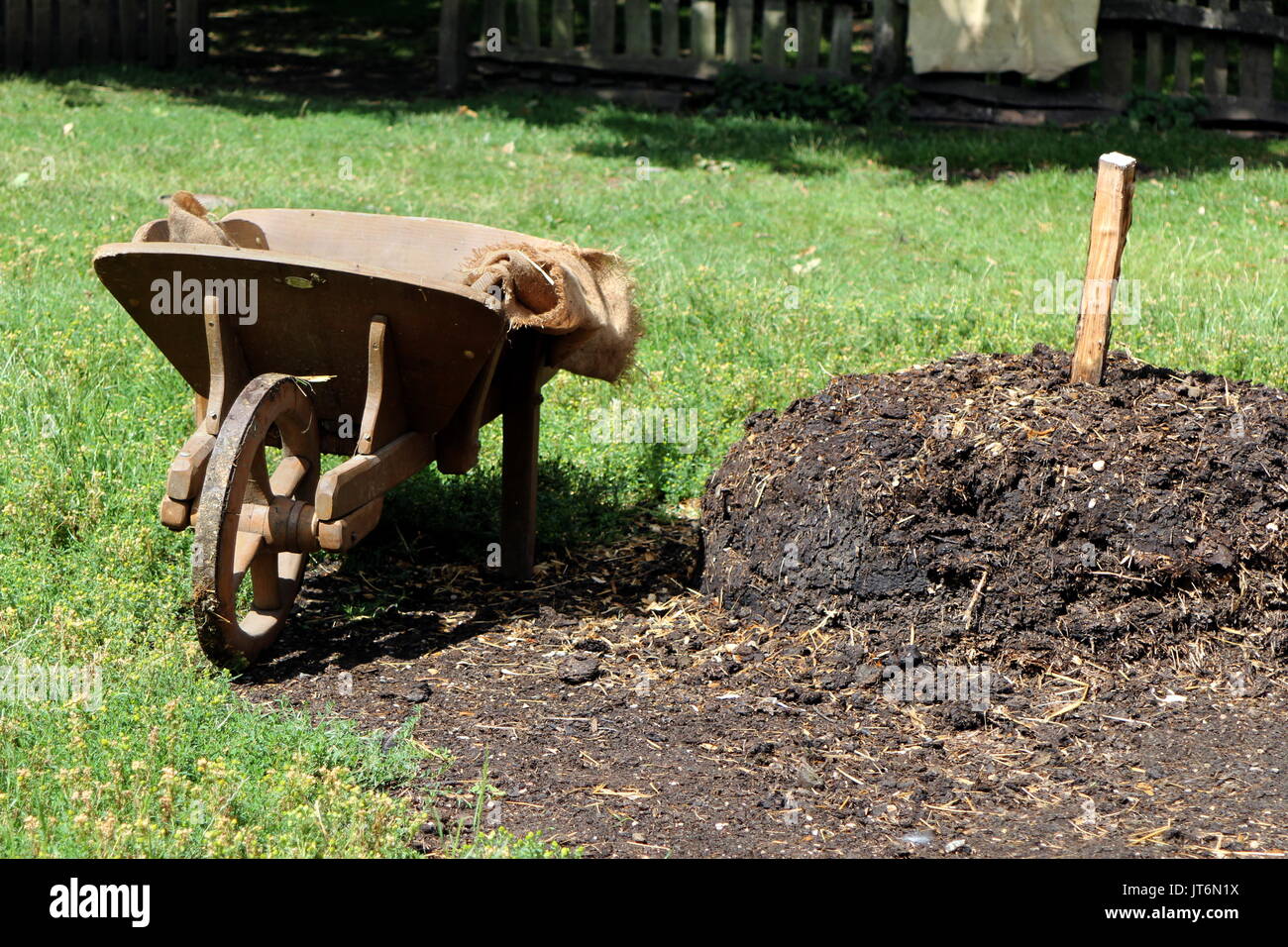Old wooden wheelbarrow next to a large pile of manure Stock Photo