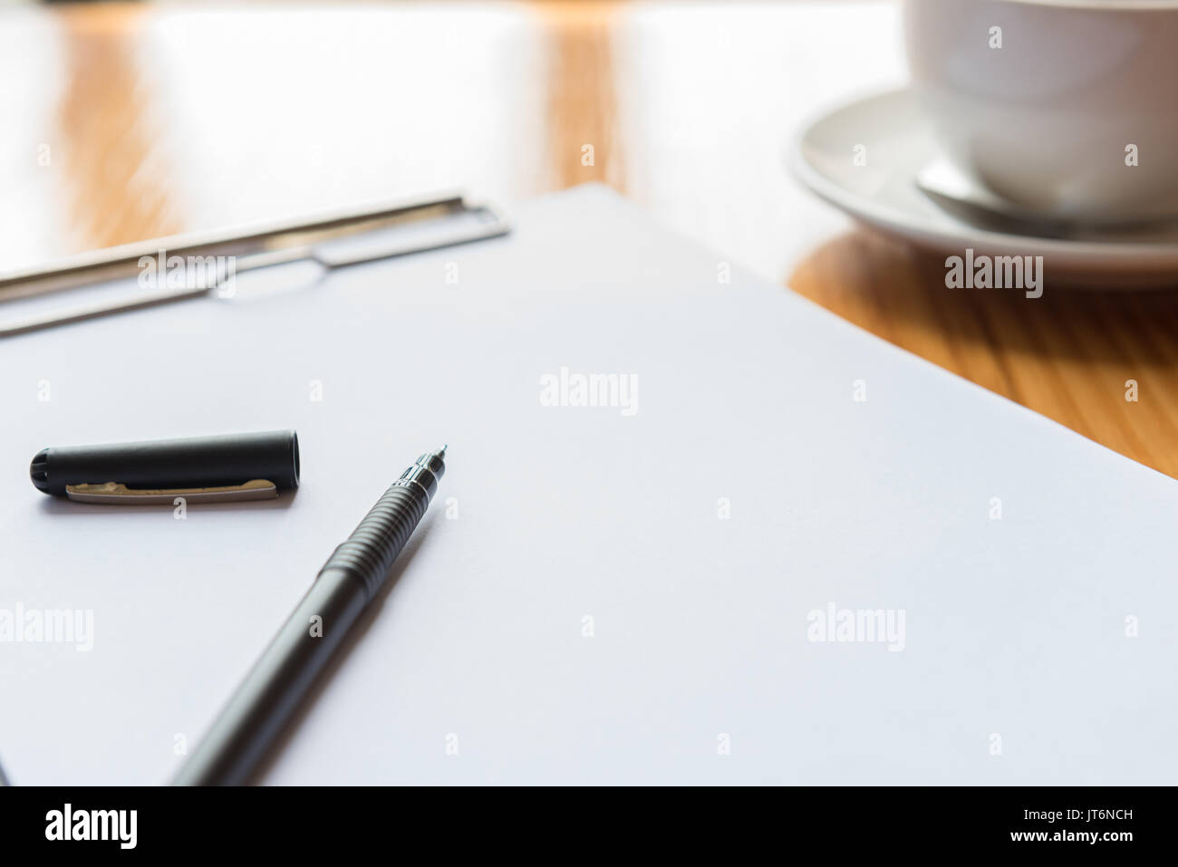 A cup of tea or coffee and a pen and notebook on wooden desks in office Stock Photo