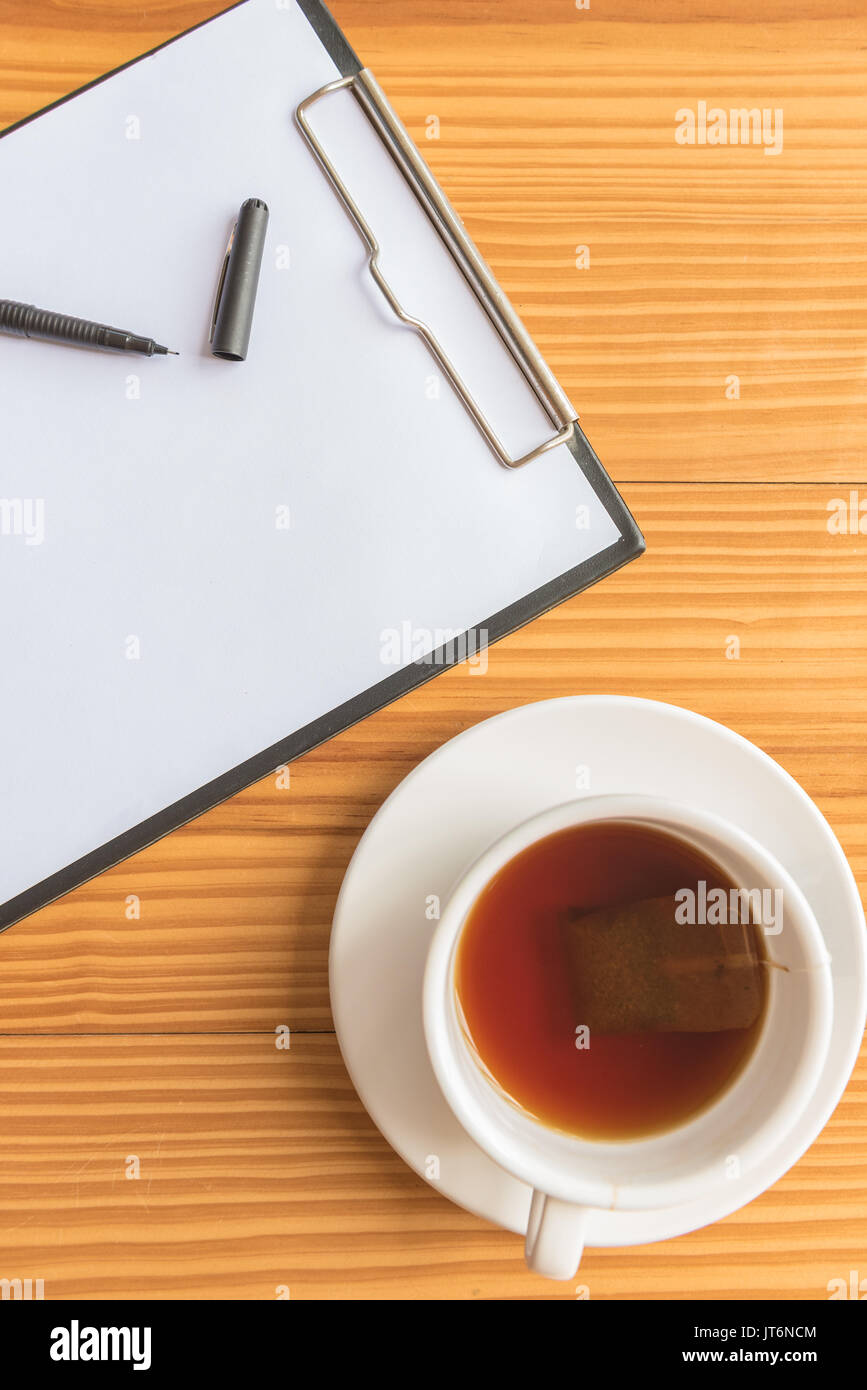 A cup of tea or coffee and a pen and notebook on wooden desks in office Stock Photo