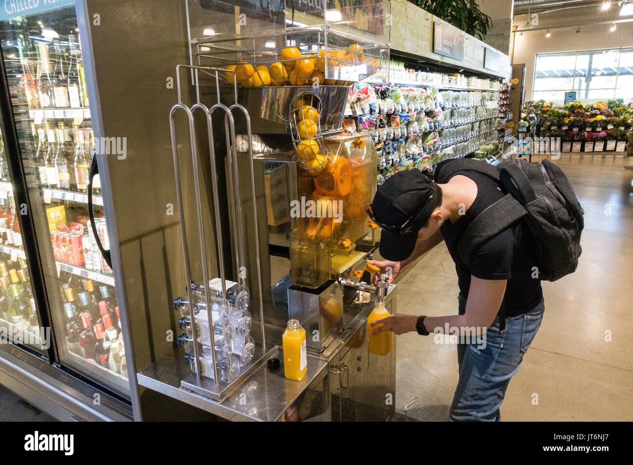 Young woman operating a self served orange juicer - fresh squeezed orange juice at the Whole Food Market store Stock Photo