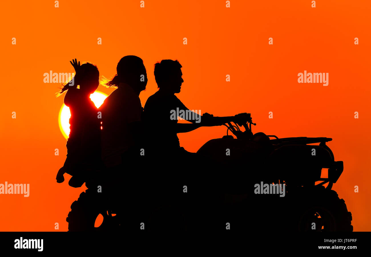 Quad bike is an ATV with three people riding silhouetted against the sunset sky having fun. Stock Photo
