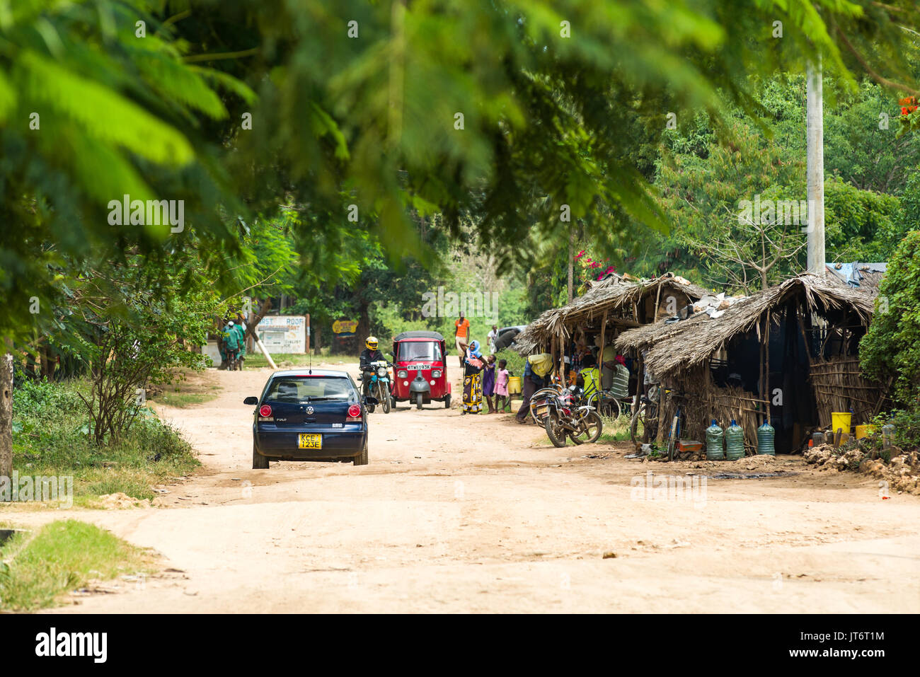 A car drives down a beach road with stalls on the roadside, Diani, Kenya Stock Photo
