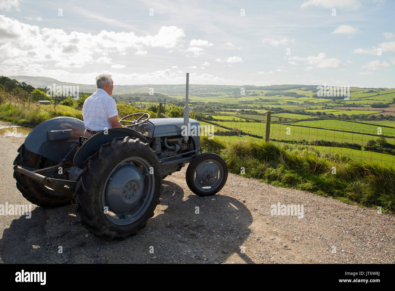 Farmer reminiscing on old tractor looking at farmland landscape Stock Photo