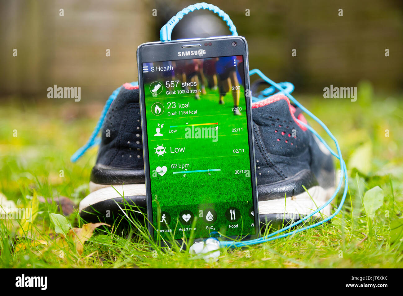 London, UK. Samsung smartphone running exercise tracking app in front of pair of running shoes with sports headphones plugged in. Stock Photo