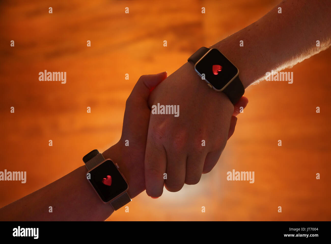 A couple hold hands whilst with hearts on their smart watches against a wooden background. Stock Photo