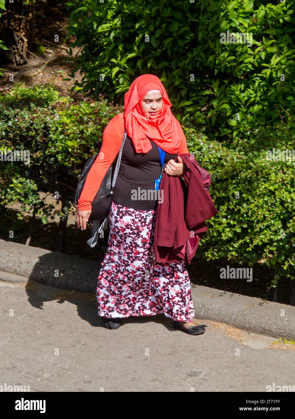 Young Muslim woman, wearing colourful head scarf and skirt walking along street in city of York, England Stock Photo
