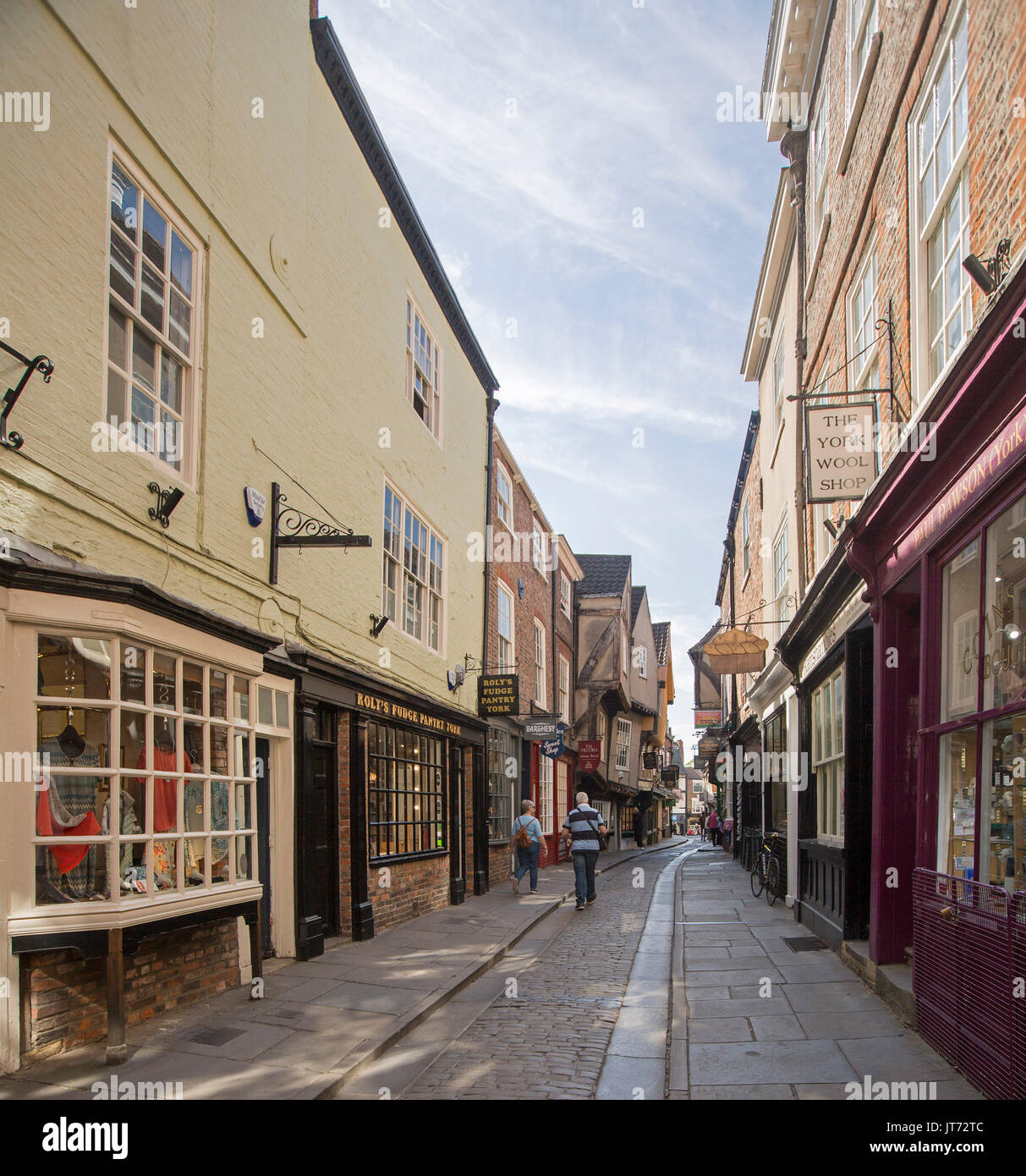 Historic shops lining ancient narrow cobbled street in The Shambles in city of York, England with pedestrians wandering along Stock Photo