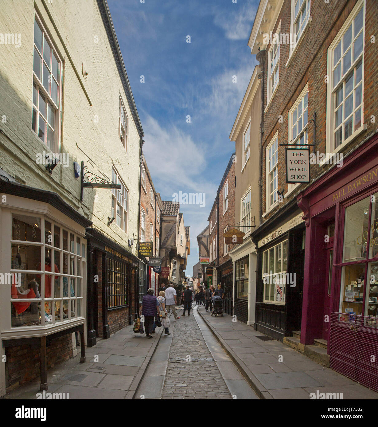 Historic shops lining ancient narrow cobbled street in The Shambles in city of York, England, with pedestrians wandering by. Stock Photo