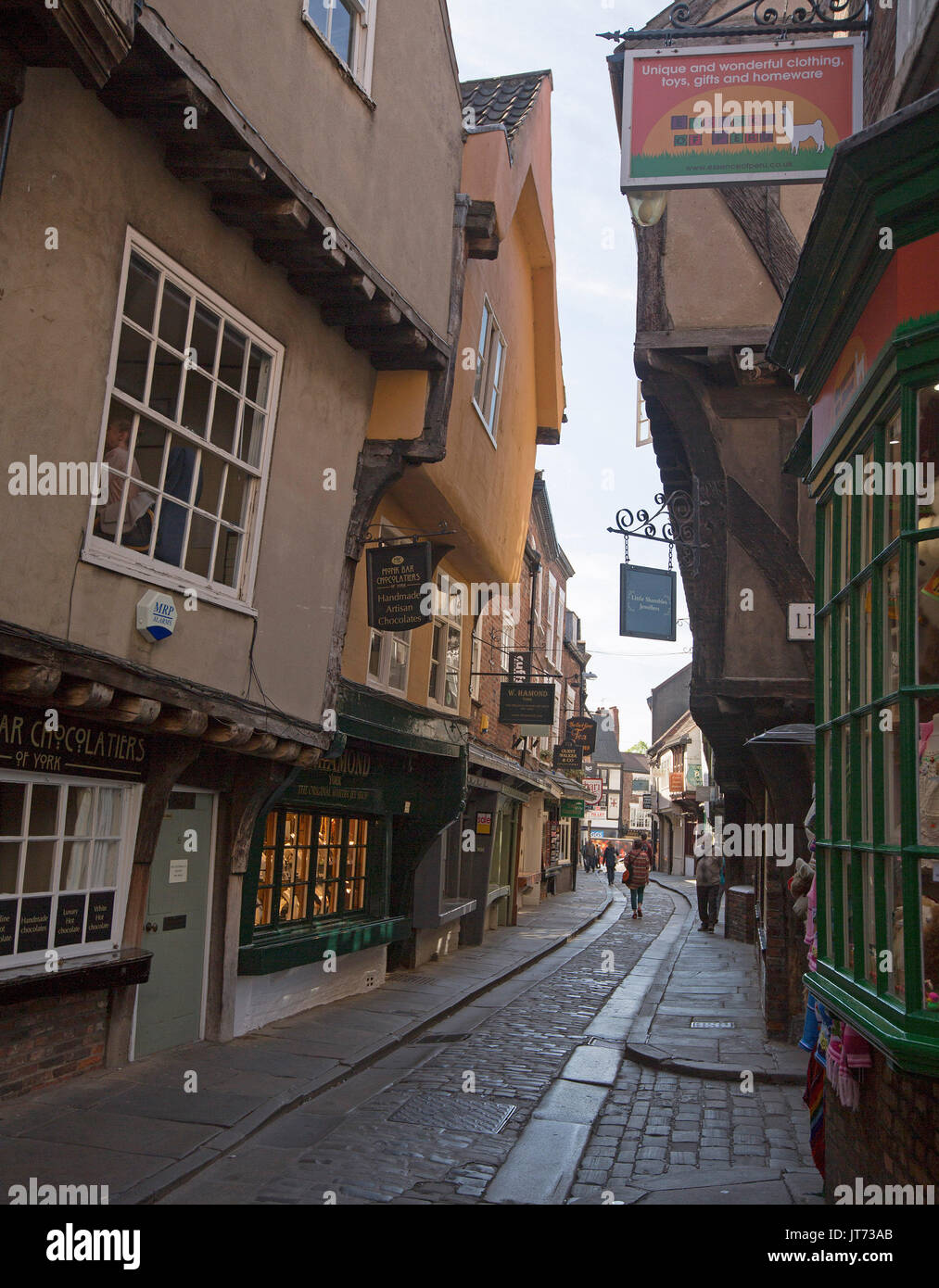 Historic shops lining ancient narrow cobbled street in The Shambles in city of York, England, with pedestrians wandering by. Stock Photo