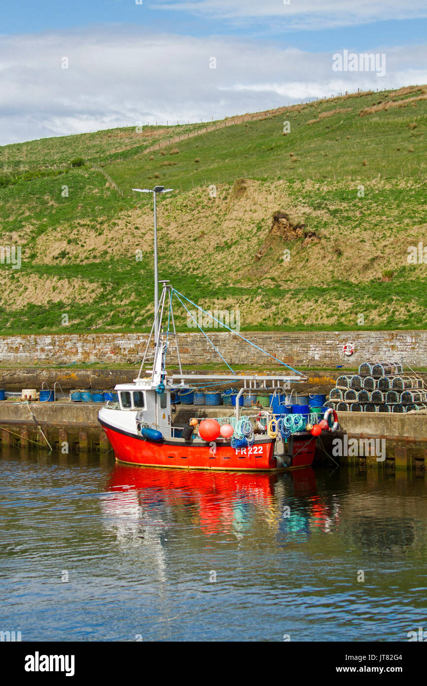 Red lobster fishing boat, beside stack of lobster pots, on calm water of sheltered harbour at Lybster, Caithness, northern Scotland Stock Photo