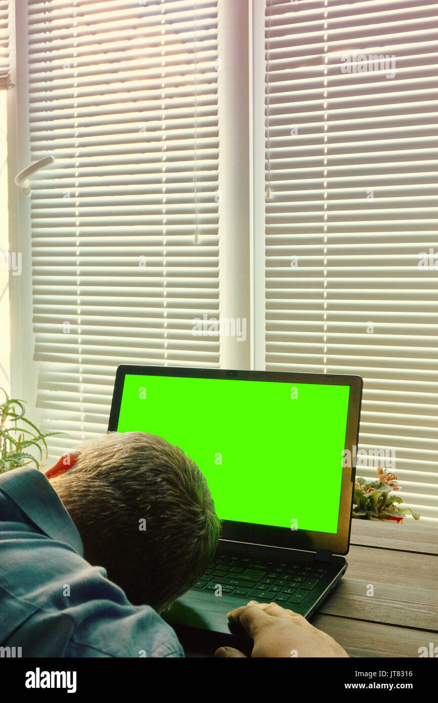 concept image of overtime work. tired man fall asleep while working on a laptop till sunrise. mans head laying on a laptop keyboard. laptop with green Stock Photo