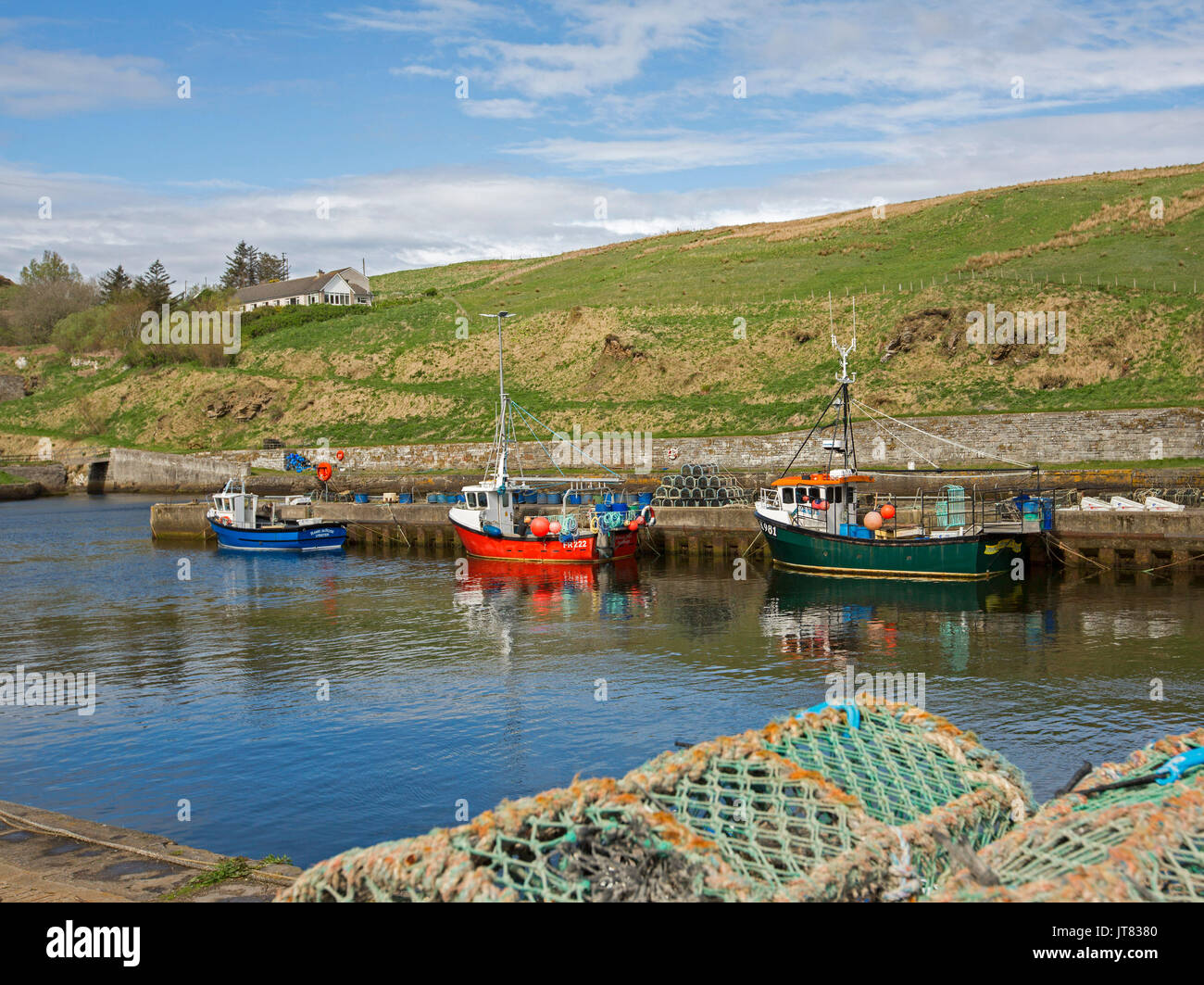 Colourful fishing boats on blue water of sheltered harbour under blue sky at village of Lybster, Caithness, northern Scotland Stock Photo