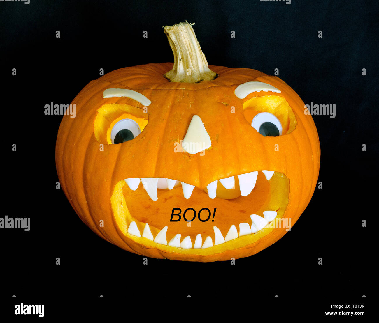 This scary Jack-o'-lantern face that was cut into a hollowed-out orange pumpkin was enhanced with sun-bleached white seashells for teeth, nose and eyebrows, plus a pair of plastic toy eyes. (The black 'BOO!' was added digitally to the image.) Carving jack-o'-lanterns is a tradition for Halloween, which evolved from All Hallows' Eve and continues to be celebrated annually on October 31. Stock Photo